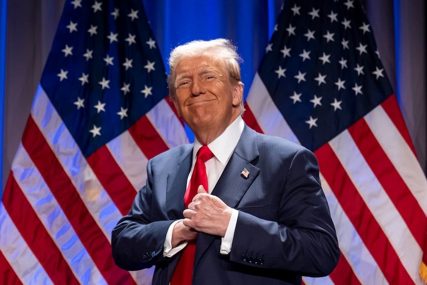 Donald Trump in front of a wall of American flags.