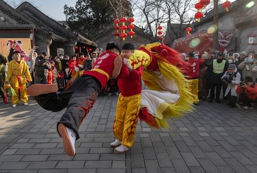 Two dancers in costume hold each other's  arms as one stands and one spins, his feet in the air