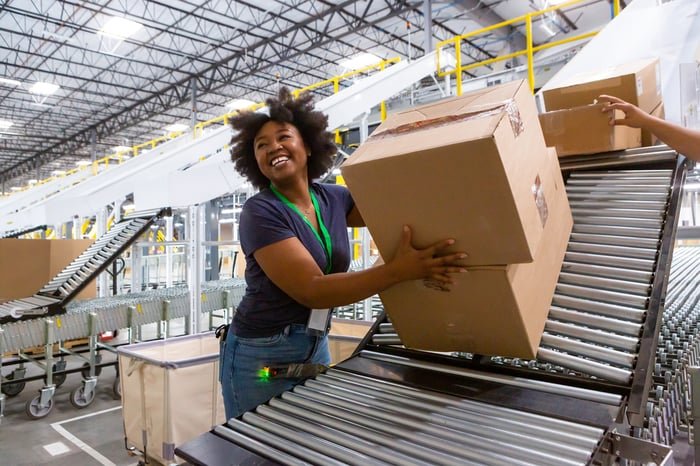 A person smiling while taking a package off of a conveyer belt.