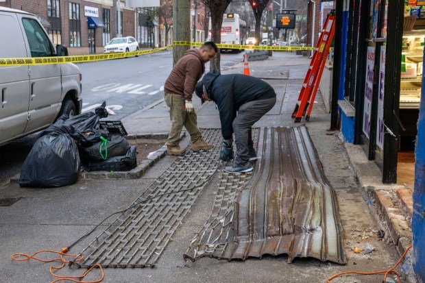 Men work on the damaged roll down security gate of the Frutas and Abarrotes Mexico 2 Deli on Victory Blvd. in Staten Island on Saturday, March 15, 2025, a day after two police officers responding to an emergency call lost control of their marked cruiser and slammed into the front of the Mexican restaurant. (Theodore Parisienne / New York Daily News)