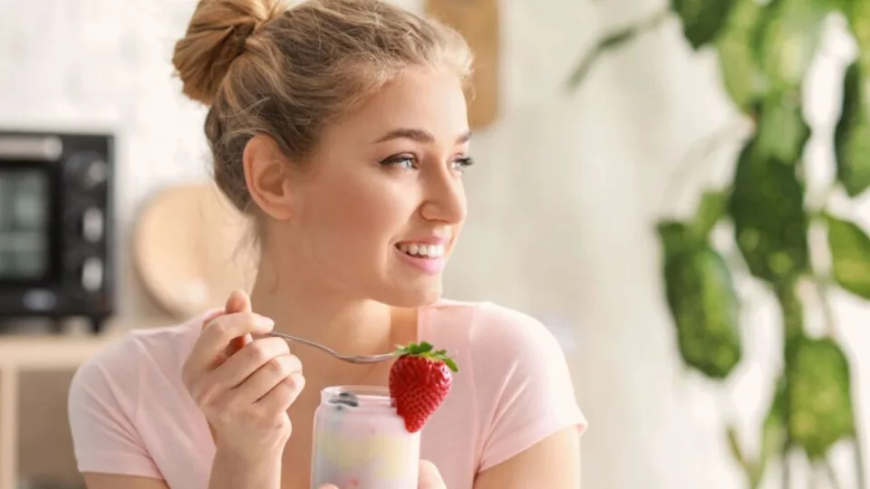 Young woman eating tasty yogurt at home