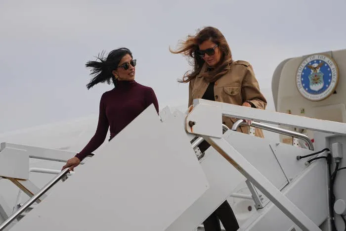 Two women in stylish outfits descend stairs from a plane, engaged in conversation
