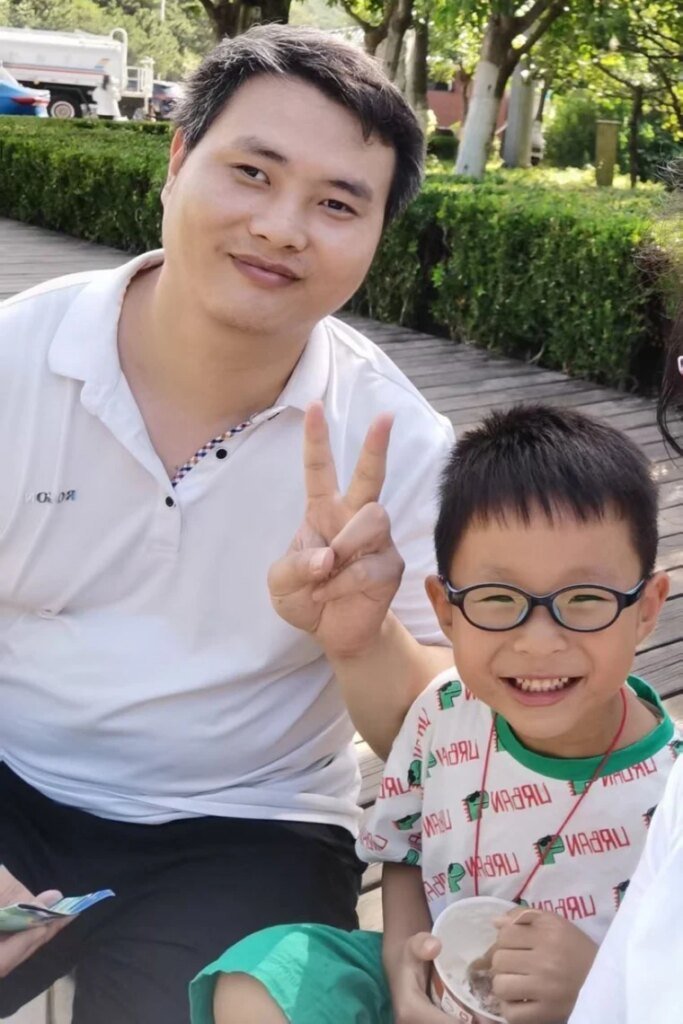 Fei Zhang poses with a peace sign next to his son, Yuanxin, while seated together outside