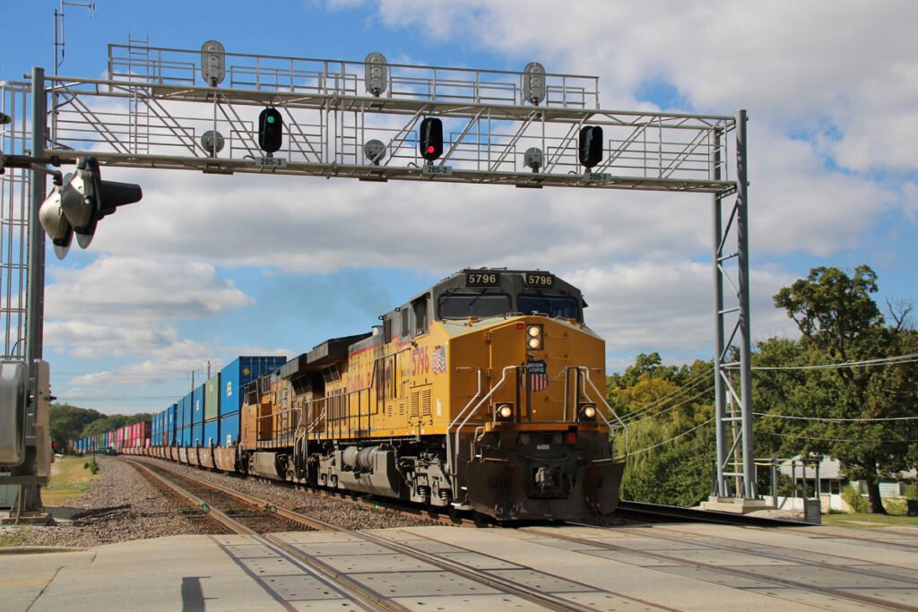 Freight train with two yellow locomotives passing under signal bridge