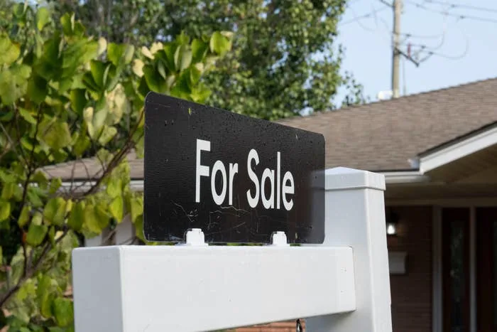 "For Sale" sign displayed in front of a house, indicating the property is on the market