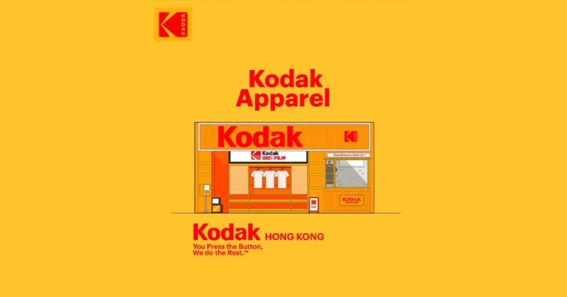 Illustration of a Kodak storefront labeled "Kodak Apparel" with shirts and film in the window, set on a yellow background. The Kodak logo appears at the top left and above the store. Text reads: "You Press the Button, We do the Rest.