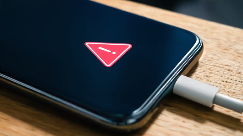 A phone sitting on a table, plugged in, with a warning logo on the screen
