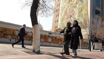 Iranian women walk past a mural depicting a famous Persian miniature, painted on the side of a building block, in Tehran on February 22, 2026. (AFP)