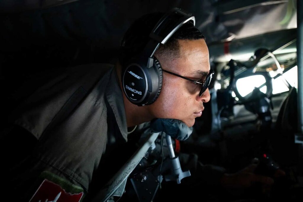 A man in uniform inside a plane, wearing sunglasses and headphones.
