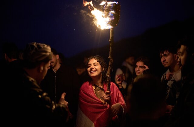 A Kurdish woman in traditional dress holds a lit torch during Nowruz, the Persian New Year, on a hill overlooking the town of Akra in the autonomous Kurdistan Region of Iraq, Friday, March 20, 2026. (AP Photo/Leo Correa)