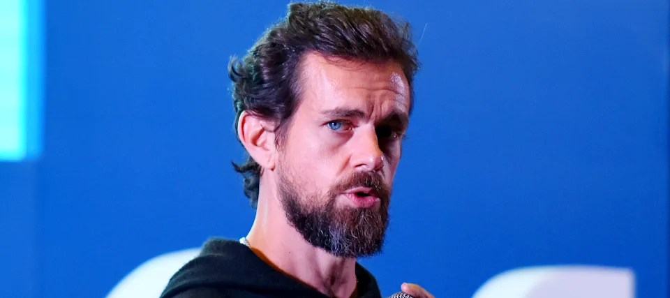 Jack Dorsey holds a microphone and looks directly at the camera.
