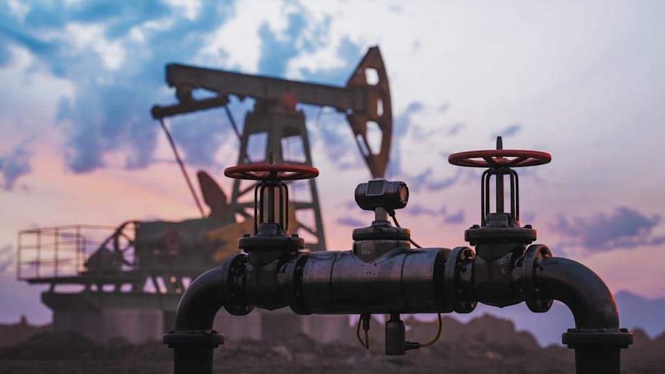 An oil pipe and valves with a pumpjack in the background.