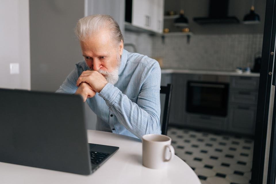 A person with a serious expression at a laptop in a kitchen.