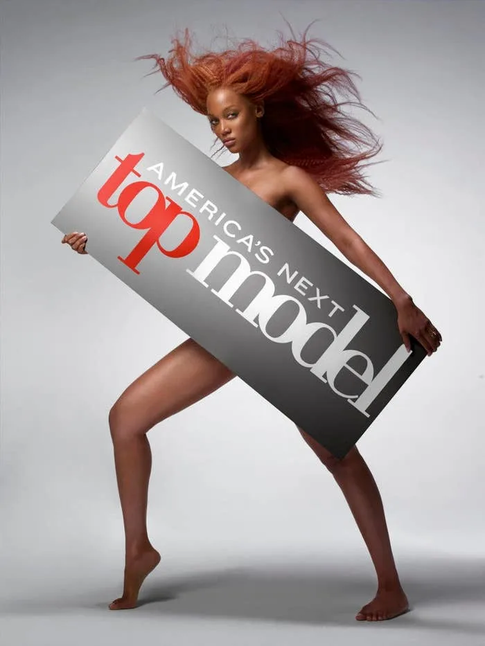 Person holding a "America's Next Top Model" sign, posing dynamically with flowing hair