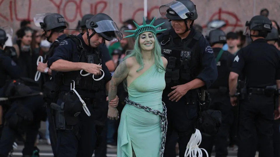 TOPSHOT - LAPD officers arrest a protester dressed as Lady Liberty in chains following clashes near the Metropolitan Detention Center during the "No Kings" national day of protest in Los Angeles on March 28, 2026. Huge crowds of protesters rallied across the United States on March 28 against President Donald Trump, venting their fury over what they see as his authoritarian style of governing, his hardline immigration policies and the war with Iran. Organizers said "at least 8 million people gathered today at more than 3,300 events across all 50 states," from big cities and small towns. US authorities provided no national crowd estimate. (Photo by ETIENNE LAURENT / AFP via Getty Images).