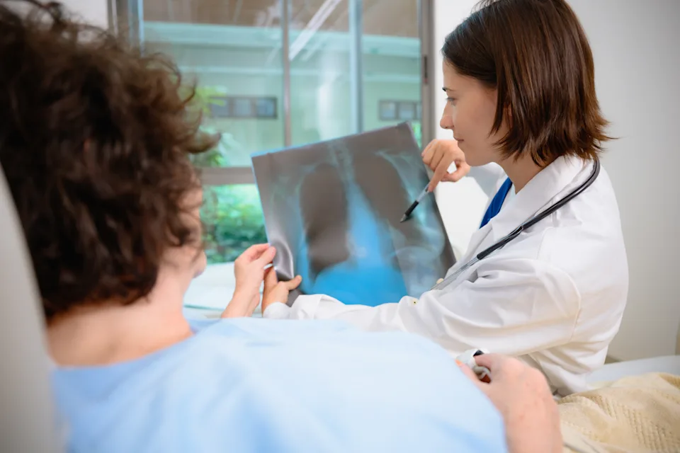 A female doctor showing X-ray film to patient with illness in hospital room and presenting a medical diagnosis to an elderly female patient as part of her health checkup.
