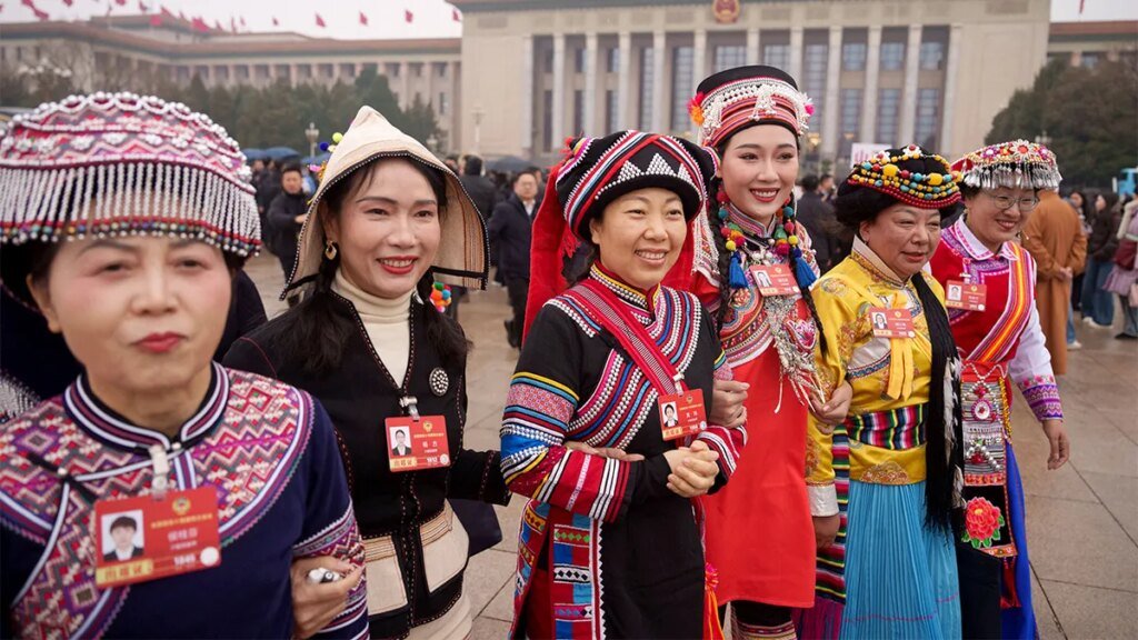 Ethnic minority representatives in traditional attire walk toward a large government building in Beijing to participate in a major annual political advisory meeting.