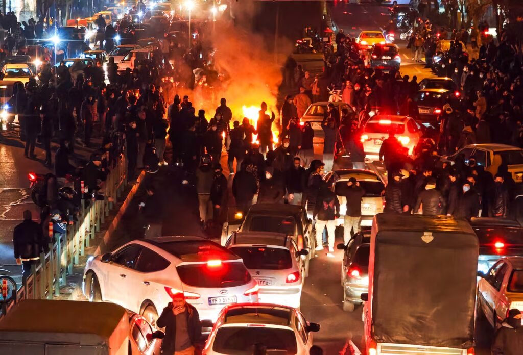 People protest at night amid a sea of cars.