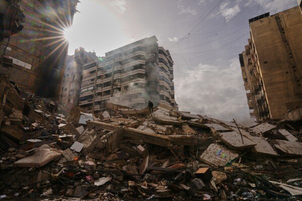 A man stands atop the rubble as smoke rises from a building destroyed in an Israeli airstrike in Dahiyeh, Beirut's southern suburbs, Lebanon, March 14, 2026. (AP Photo/Hassan Ammar)