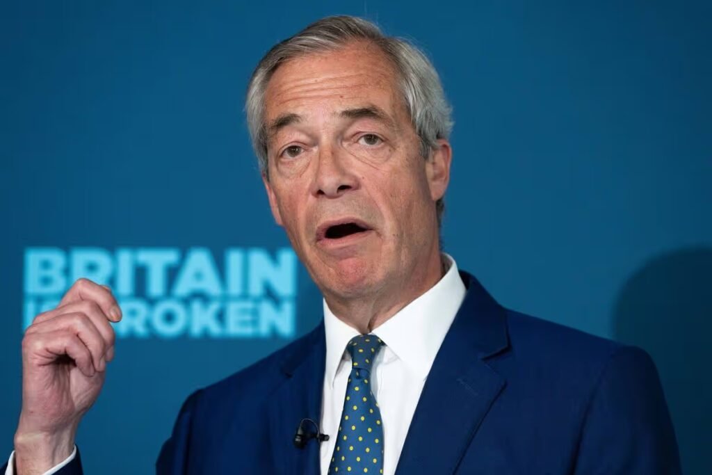 An individual, dressed formally, is engaged in a speech. The backdrop features a blue banner with the text "BRITAIN BROKEN" prominently displayed.